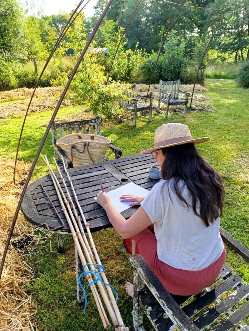Ysabel écrivant dans un carnet, attablée sous les arches du jardin