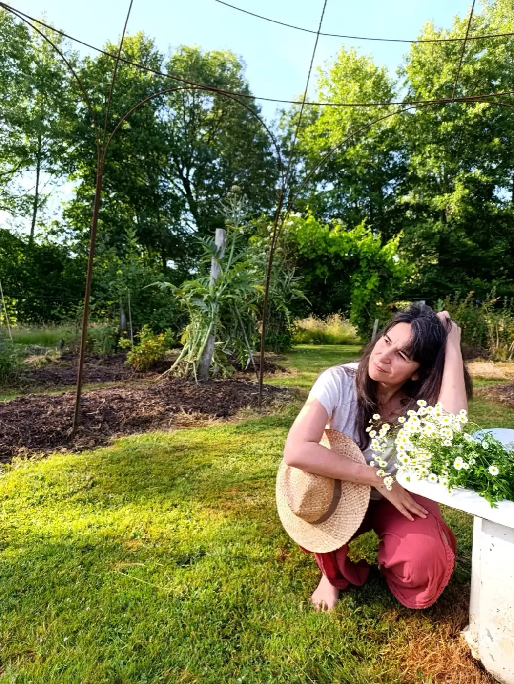 Ysabel dans son jardin, chapeau de paille à la main, dans une lumière dorée